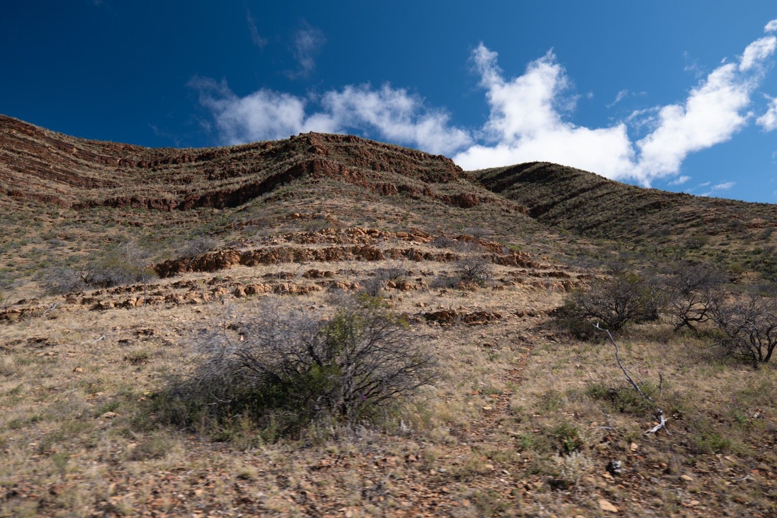 A hillside of tilted, layered rock under a blue sky with white clouds