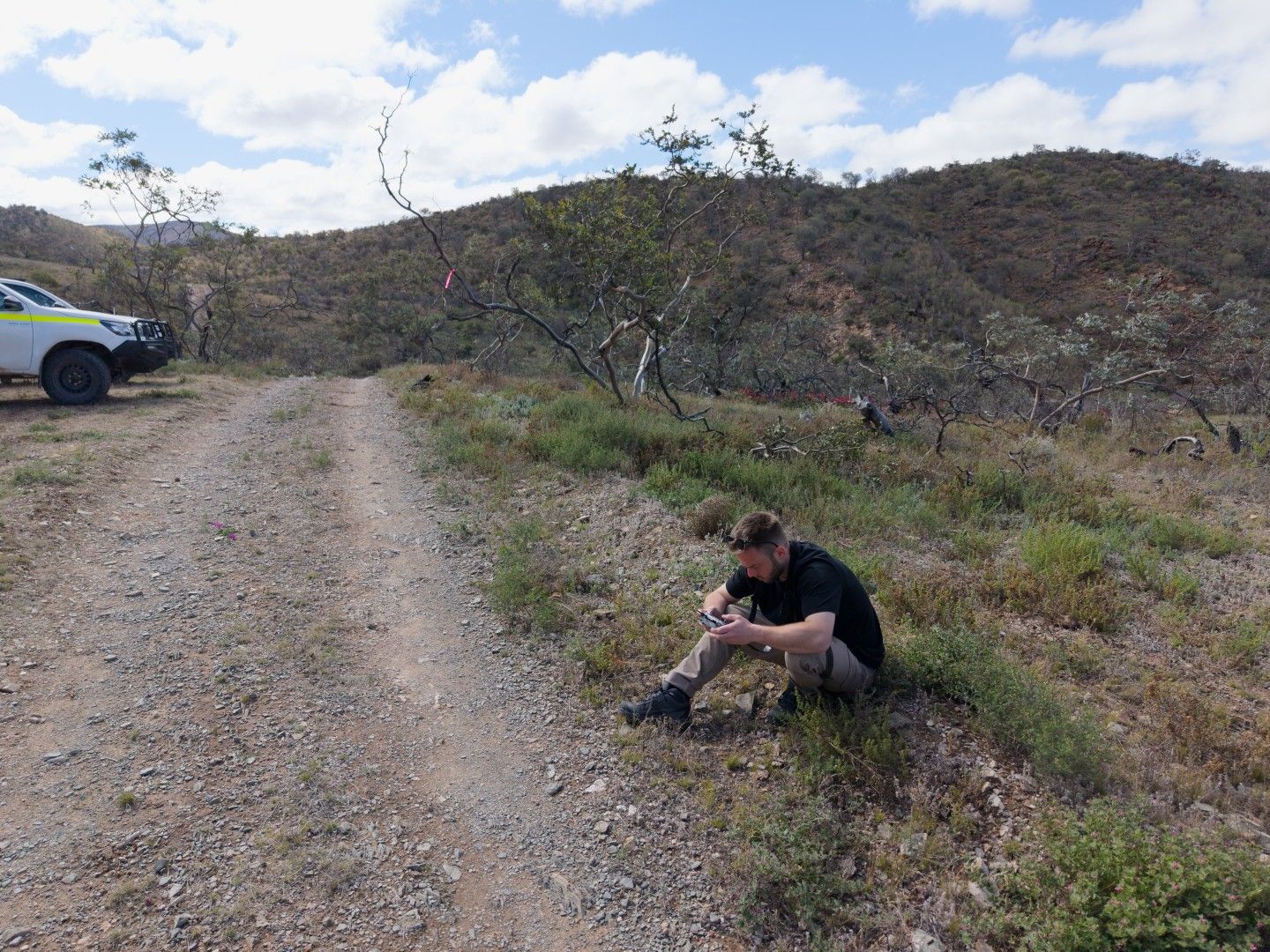 A team member sitting beside a gravel track looking closely at something in his hands