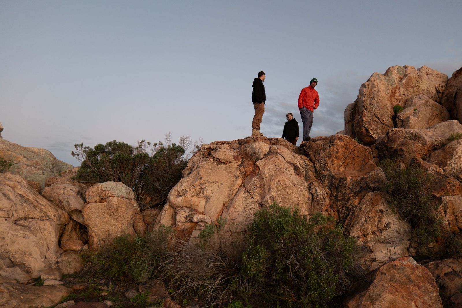 Three people standing on top of large rounded boulders at dusk