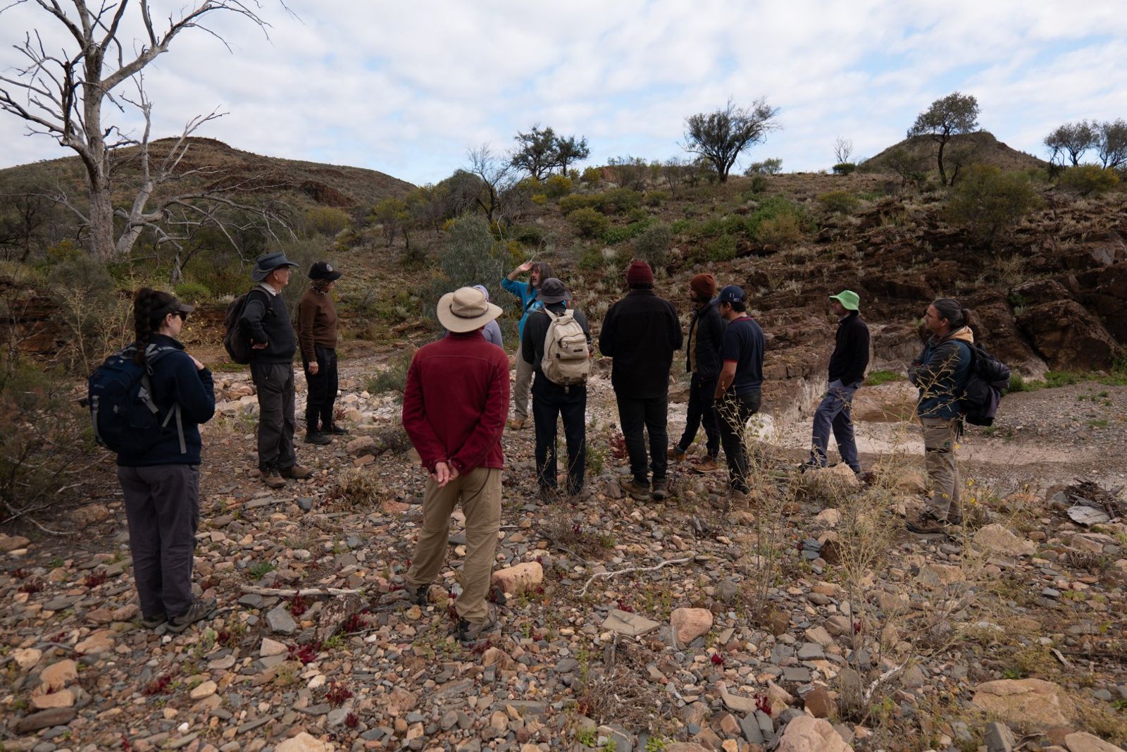 The team standing in a dry, stony creek bed with low rocky walls and gum trees