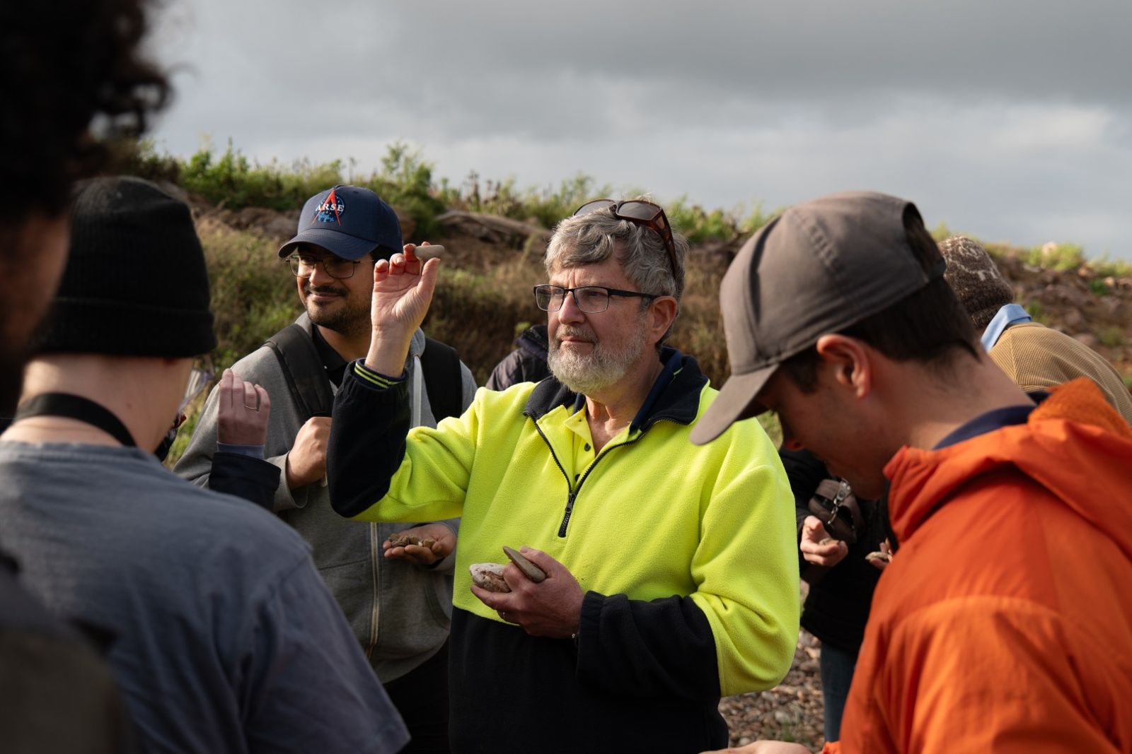 Team members gathered around, one holding up a rock and explaining it