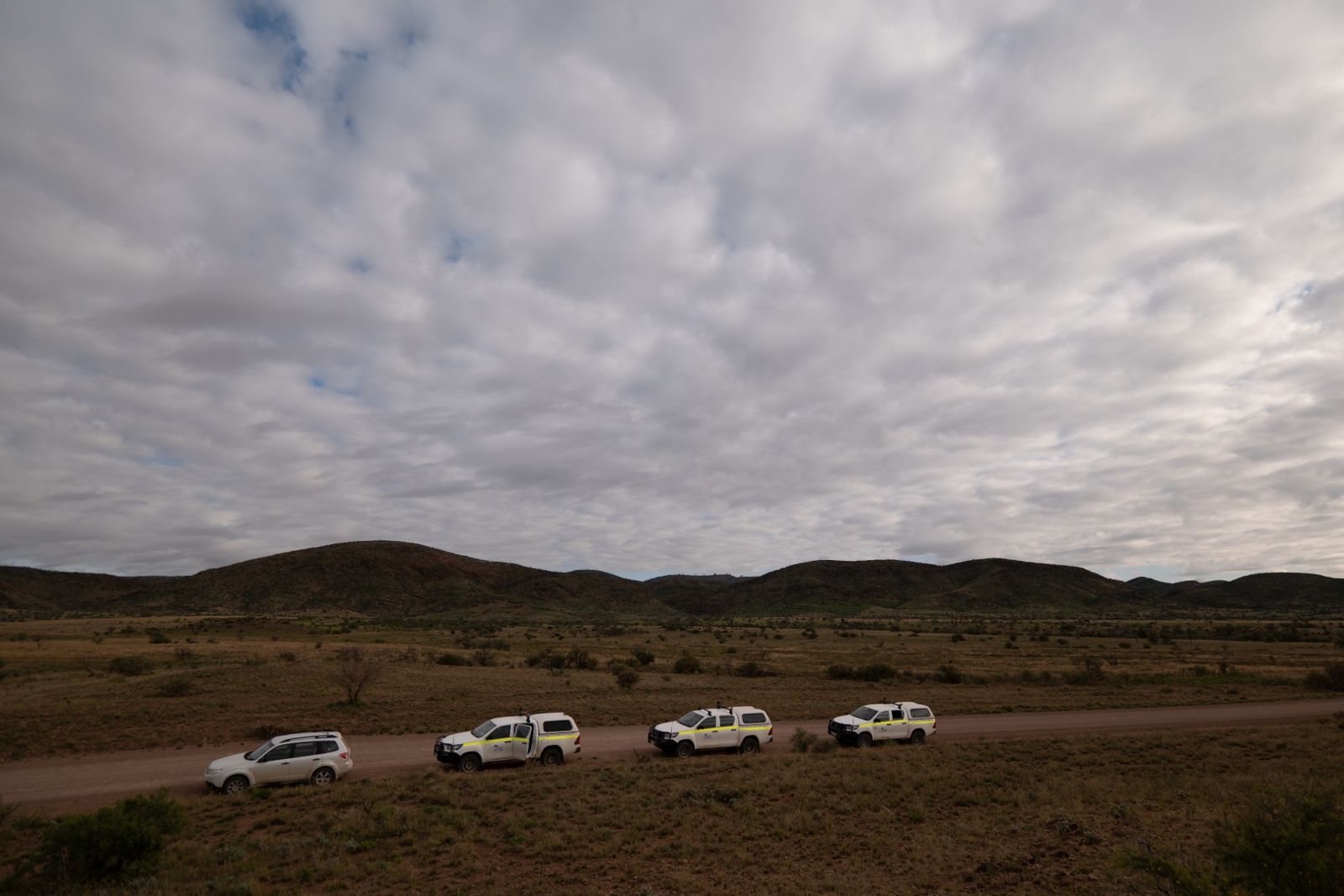 Four white 4WDs parked on a gravel road under a cloudy sky