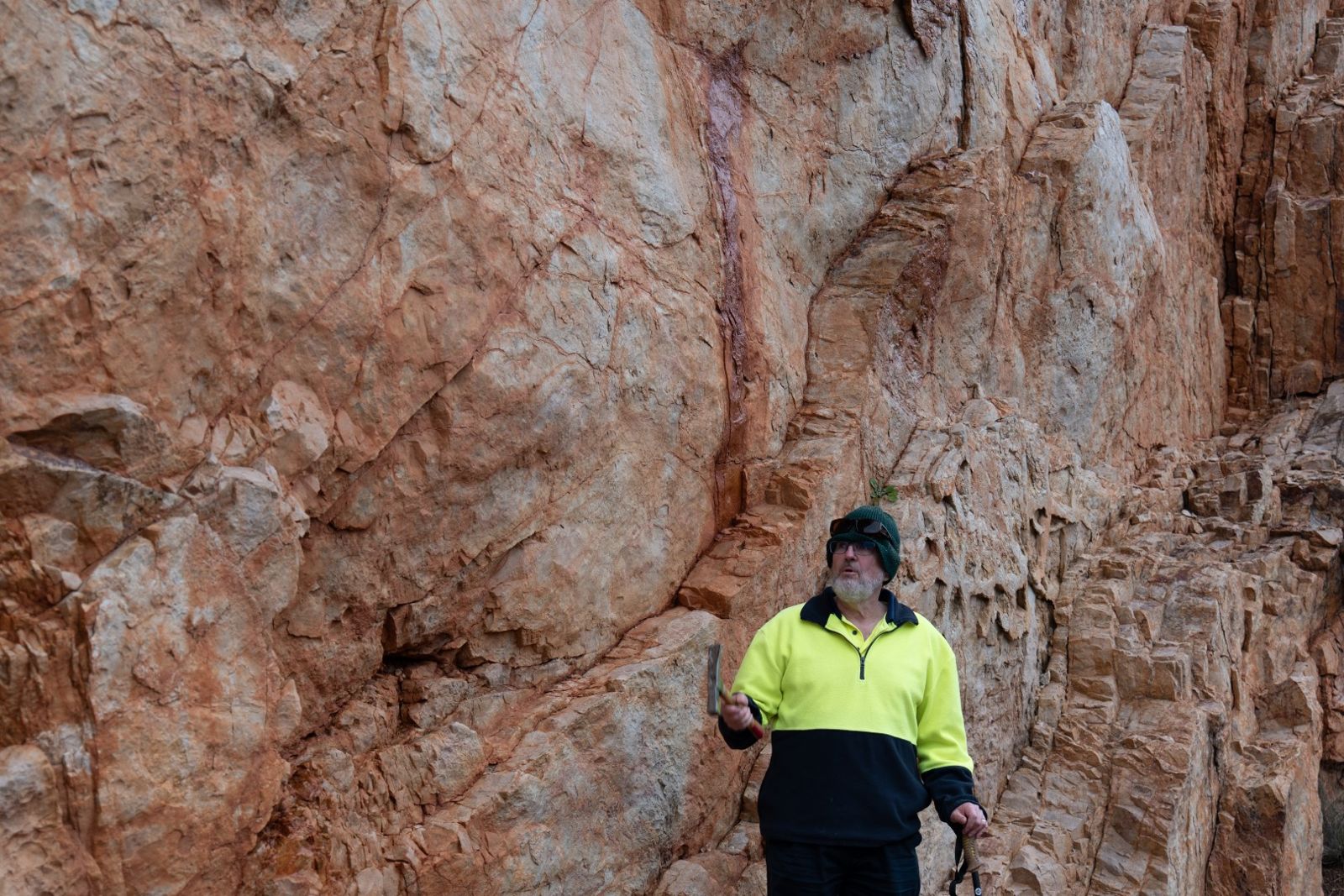 A team member in a hi-vis shirt standing in front of a cracked, weathered rock face
