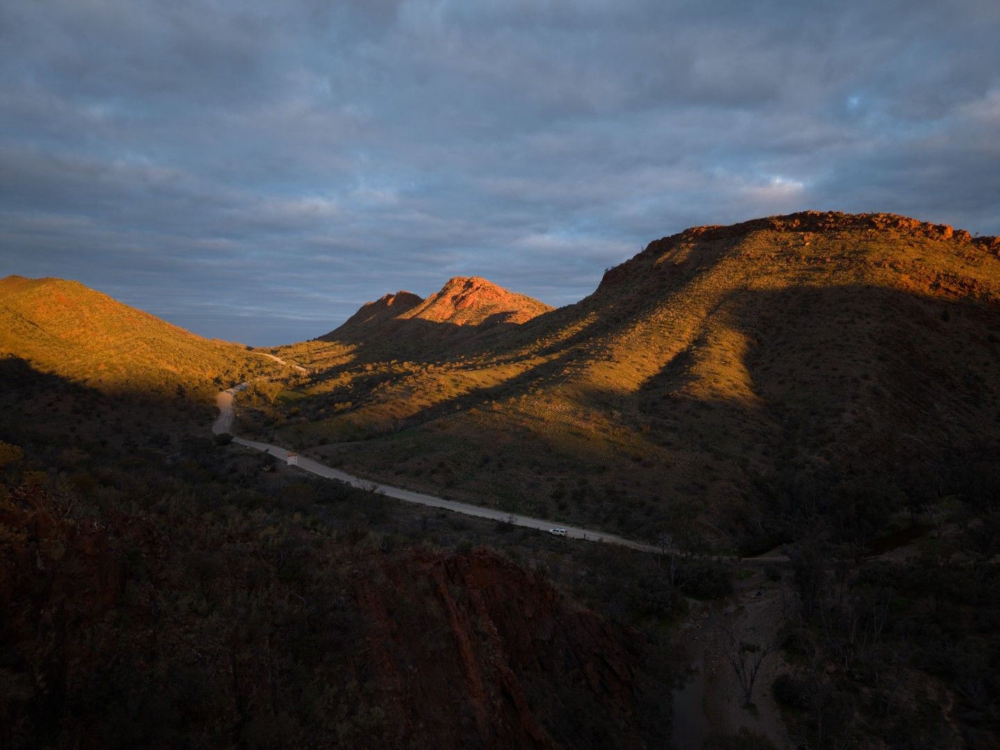 Aerial view of ridges lit orange by the evening sun, with a winding track below, near The Pinnacles at Arkaroola