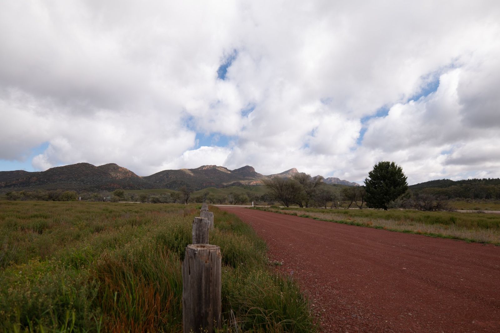 A red dirt road and fence line running towards the ranges under a cloudy sky
